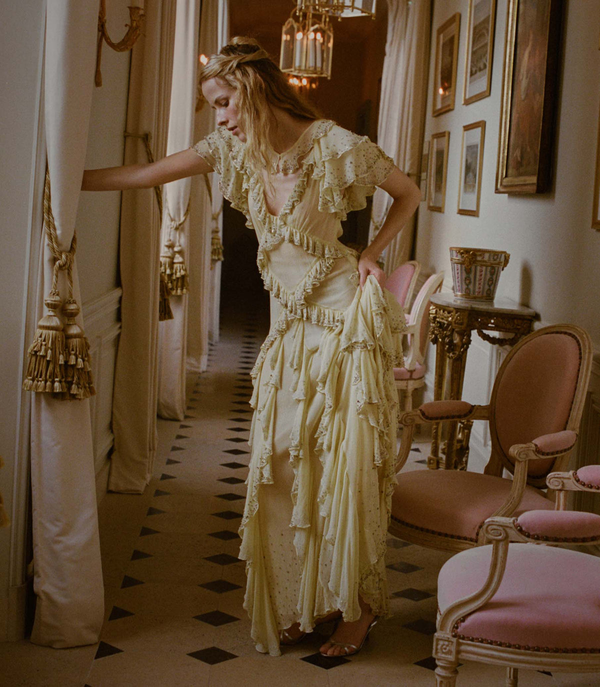 Woman in a vintage-style yellow dress standing in an elegant room with ornate decor.