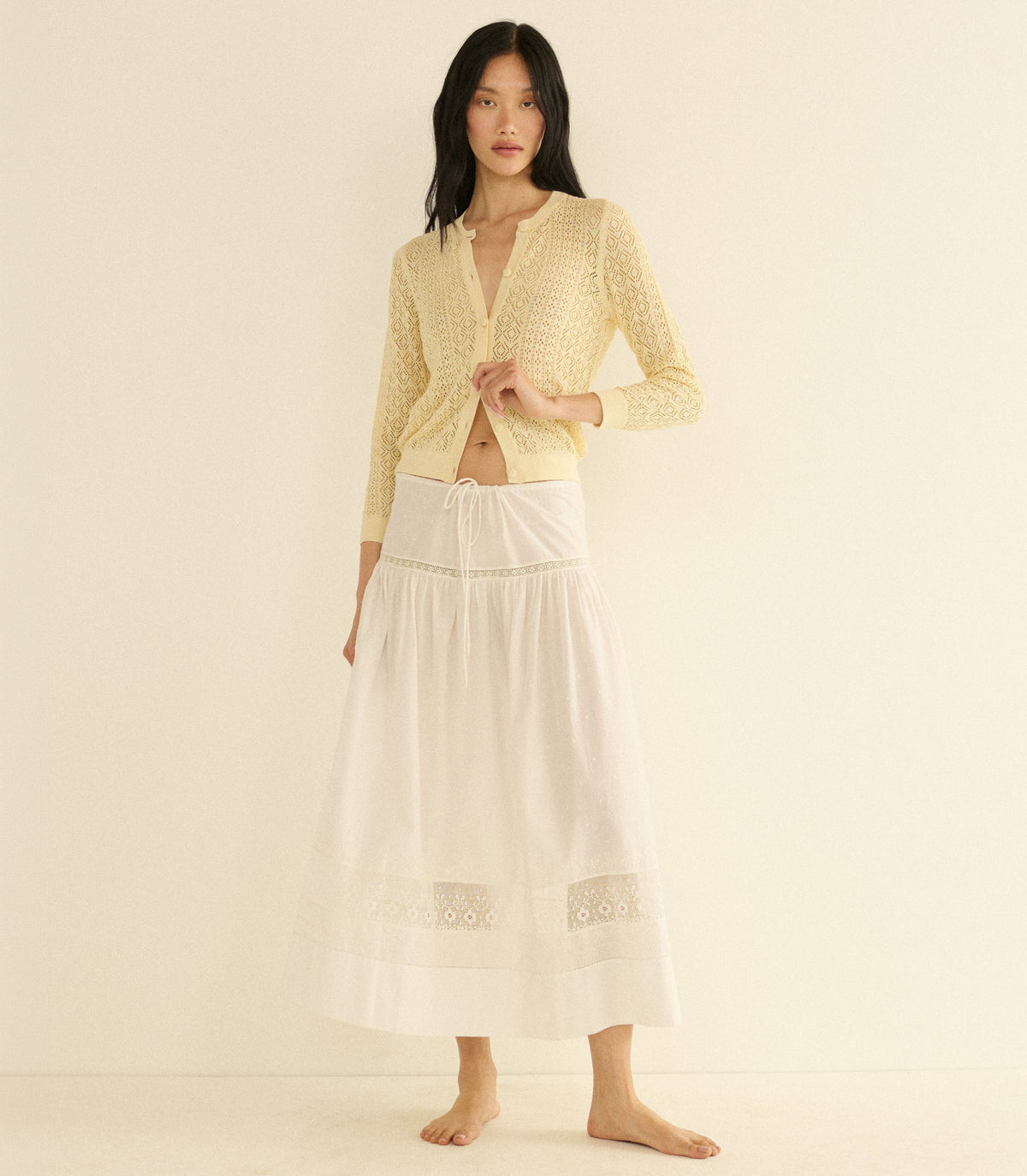 Woman wearing a cream cardigan and a white skirt on a beige background
