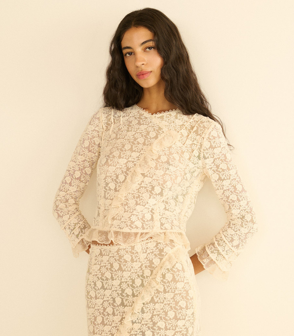 Woman wearing a cream lace outfit against a plain background