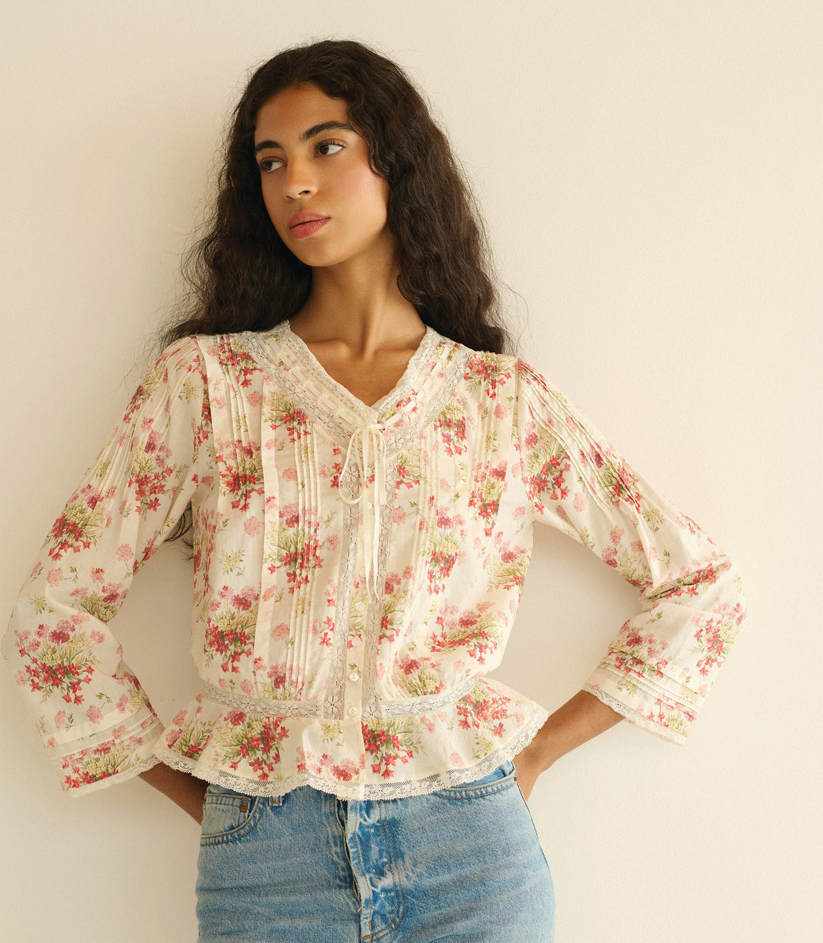 Woman wearing a floral blouse and denim pants against a plain background